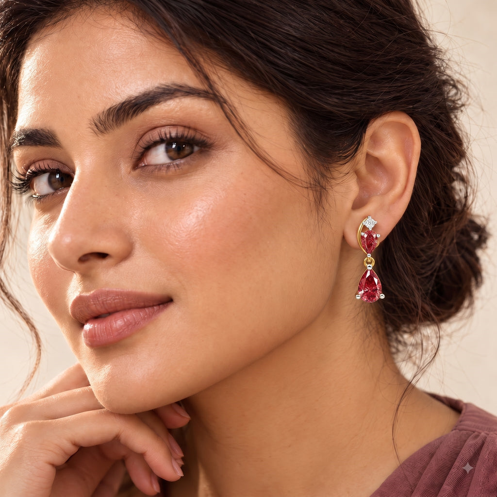 A close-up of a woman wearing a gold drop earring with two red teardrop-shaped gemstones and a small clear stone at the top.