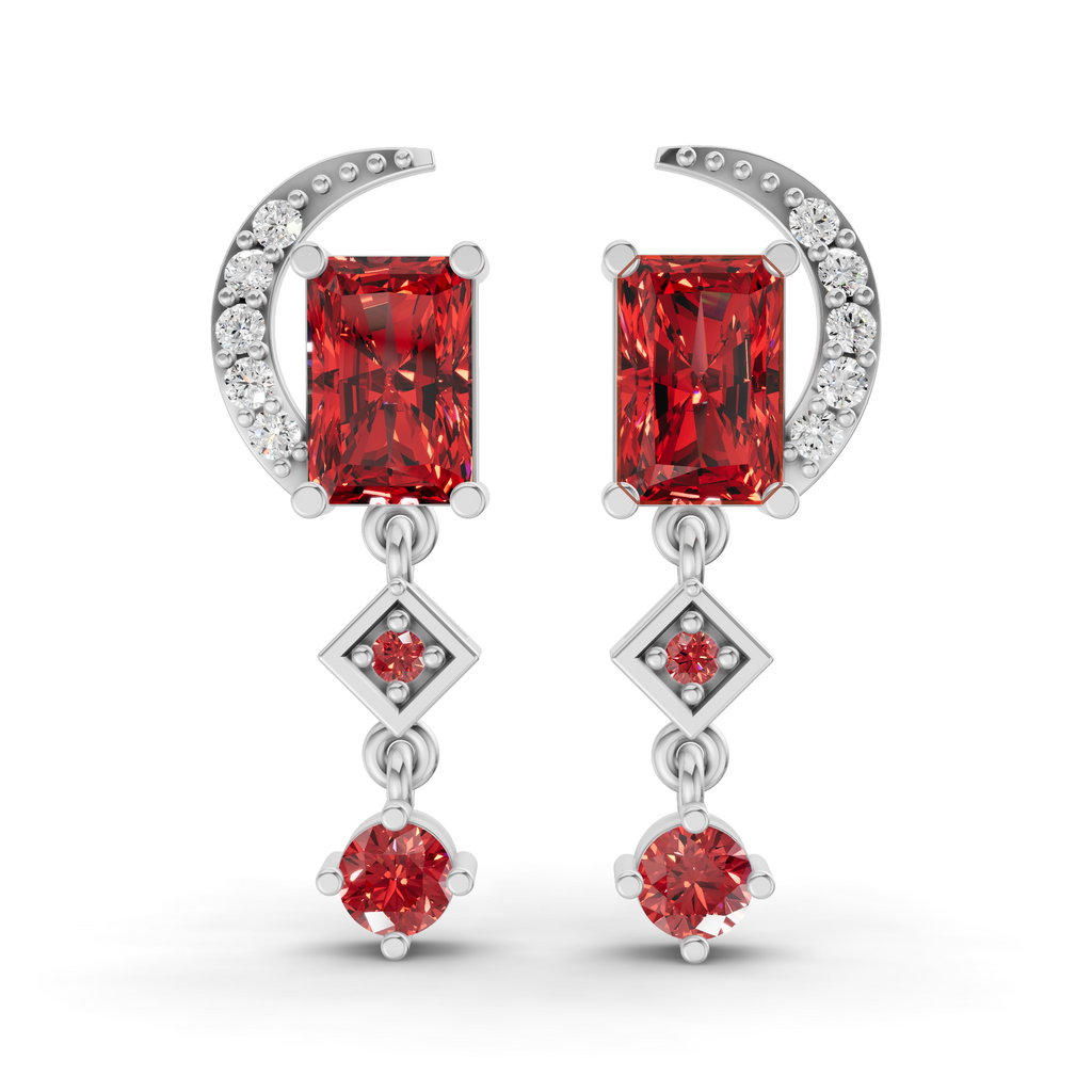 A pair of silver drop earrings featuring rectangular red gemstones, a crescent moon with small clear stones, and diamond-shaped drops with smaller red gemstones, shown on a white background.