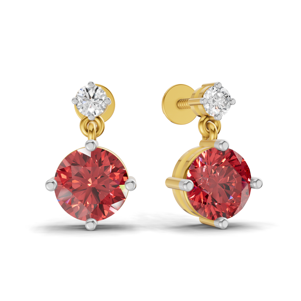 A pair of gold drop earrings featuring a large round red gemstone in a four-prong setting, with a smaller round clear gemstone at the top and a visible post/back on one earring, shown on a white background.