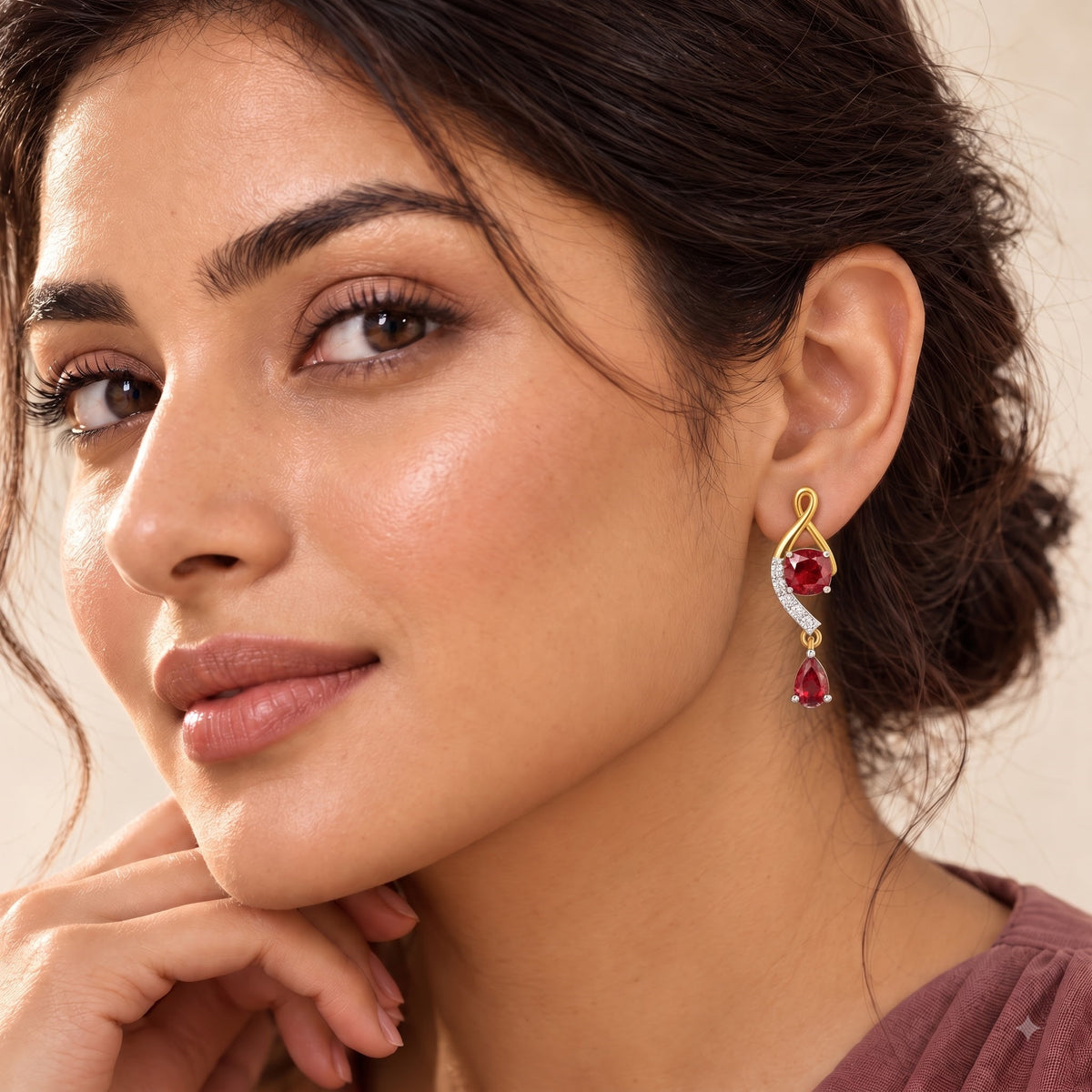 A close-up lifestyle shot of a woman wearing a gold and white stone drop earring with a red teardrop gemstone, set against a soft beige background.