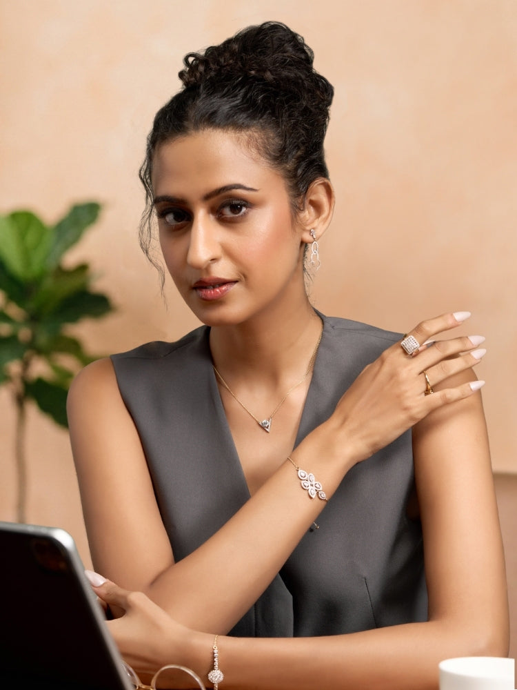 Woman wearing jewelry, including a ring and bracelet, against a beige background.