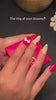 A hand with styled acrylic nails opens a small, bright pink SparQ jewelry box to reveal a gold ring featuring a cushion-shaped halo setting with a central gemstone, with overlay text that reads "The ring of your dreams💍".